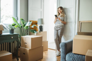 Mature woman moves in to new home, unpacking boxes and enjoying in her new home. She is resting and using smart phone.